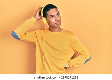 Young African American Guy Listening To Music Using Headphones Confuse And Wondering About Question. Uncertain With Doubt, Thinking With Hand On Head. Pensive Concept. 