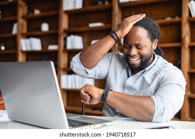 Young African American Guy Totally Forgot About A Business Meeting, Sitting At The Desk And Working On Laptop, Checking The Time From A Watch On His Wrist, Time To Take Pills, Time For Changes Concept