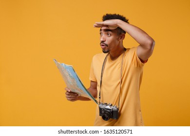 Young african american guy in t-shirt with vintage photo camera posing isolated on yellow orange background. People lifestyle concept. Hold city map, hold hand at forehead looking far away distance - Powered by Shutterstock