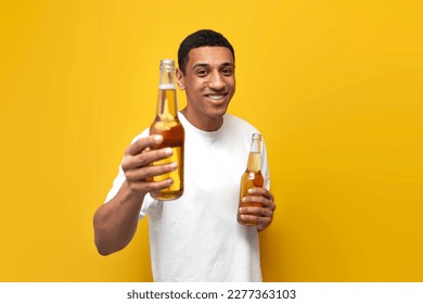 young african american guy in white t-shirt holds two bottles of beer on yellow isolated background, man offers to drink alcohol - Powered by Shutterstock