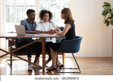 Young African American husband and wife sit at desk talk with female real estate agent discuss buying house together, biracial couple meet with designer architect or broker consult in modern office - Powered by Shutterstock