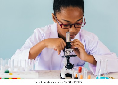 Young African American kid using microscope and experimenting scientific lab along with chemical substance tubes and flasks in classroom - science and learning education concept - Powered by Shutterstock