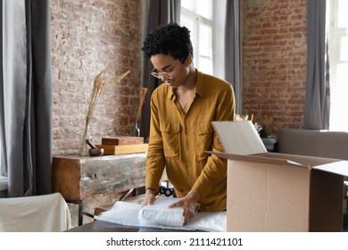 Young African American logistic employee woman packing goods, wrapping, putting books into cardboard carton box, preparing parcel for sending, transportation, collecting donations - Shutterstock ID 2111421101
