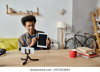 A young African American male blogger is sitting at a table with a tablet in front of him, discussing into a phone camera. - Powered by Shutterstock