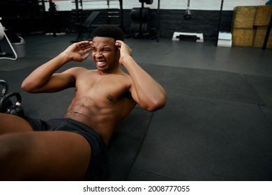 Young African American Male Doing Sit-ups On The Floor In The Gym. Mixed Race Male Personal Trainer Exercising Shirtless Indoors. High Quality Photo