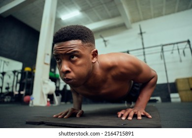 Young African American Male Doing Push-ups In The Gym. Mixed Race, Male Personal Trainer Doing Cross Fit Indoors. High Quality Photo