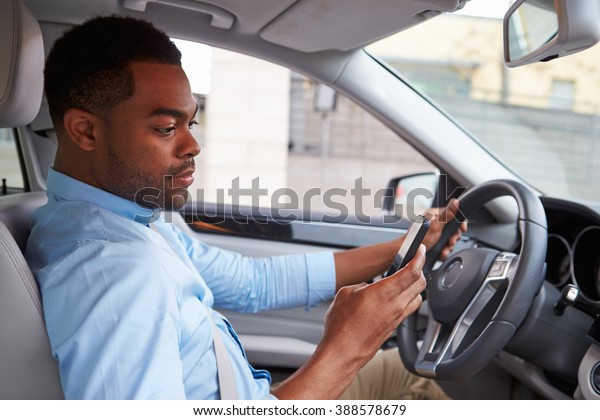 Young African American male driver using phone, in\
car view
