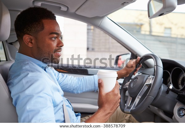 Young African American male driver with coffee, in\
car view