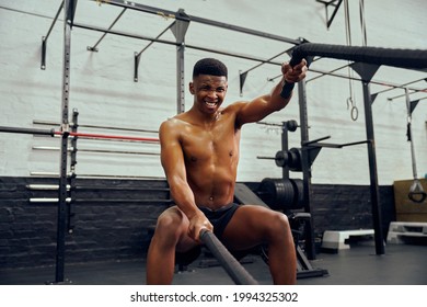 Young African American Male Exercising Inside A Gym. Topless Male Personal Trainer Using Rope To Strengthen His Arms. High Quality Photo