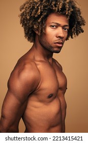 Young African American Male With Naked Torso And Curly Hair Looking At Camera Against Brown Background