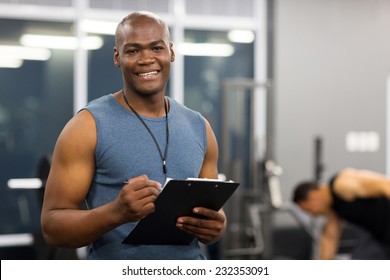 Young African American Male Personal Trainer Holding Clipboard In Gym