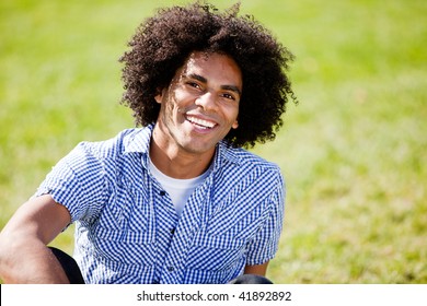 A young African American male sitting on the grass
