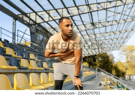 Young African American male sportsman, athlete, runner tired after training. He is standing in the stadium, bent over, holding his chest, breathing, resting. Stockfoto © 