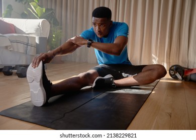 Young African American male stretching his legs and hamstrings in living room - Shutterstock ID 2138229821