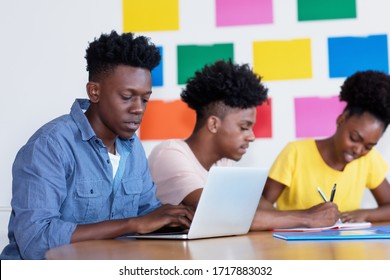 Young african american male student at computer with group of students at classroom of university or college
