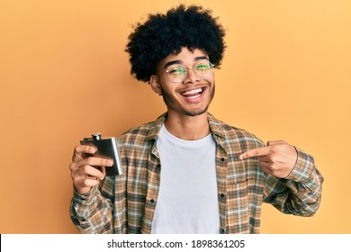 Young african american man with afro hair drinking alcohol from whiskey flask pointing finger to one self smiling happy and proud 