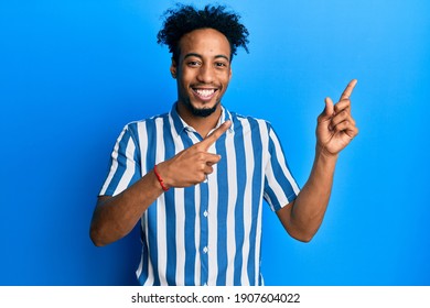 Young african american man with beard wearing casual striped shirt smiling and looking at the camera pointing with two hands and fingers to the side. 