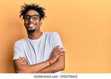 Young African American Man With Beard Wearing Casual White T Shirt And Glasses Happy Face Smiling With Crossed Arms Looking At The Camera. Positive Person. 