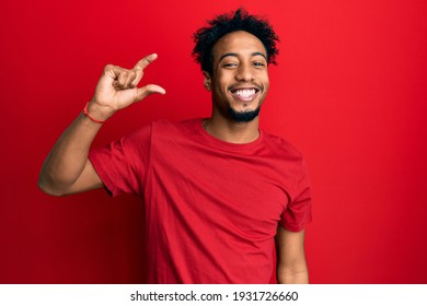 Young African American Man With Beard Wearing Casual Red T Shirt Smiling And Confident Gesturing With Hand Doing Small Size Sign With Fingers Looking And The Camera. Measure Concept. 