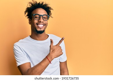 Young African American Man With Beard Wearing Casual White T Shirt And Glasses Smiling Cheerful Pointing With Hand And Finger Up To The Side 