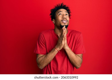 Young African American Man With Beard Wearing Casual Red T Shirt Begging And Praying With Hands Together With Hope Expression On Face Very Emotional And Worried. Begging. 