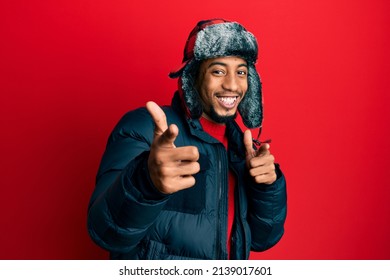 Young african american man with beard wearing winter hat and coat pointing fingers to camera with happy and funny face. good energy and vibes. 