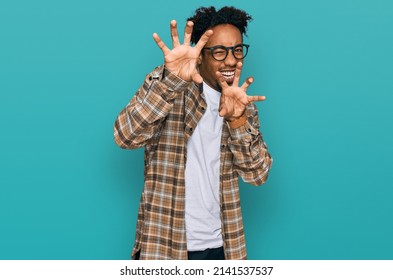 Young african american man with beard wearing casual clothes and glasses smiling funny doing claw gesture as cat, aggressive and sexy expression 