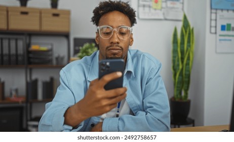 Young african american man with a beard and glasses using a smartphone in a modern office workspace with indoor plants and a bookshelf in the background. - Powered by Shutterstock