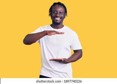 Young African American Man With Braids Wearing Casual White Tshirt Gesturing With Hands Showing Big And Large Size Sign, Measure Symbol. Smiling Looking At The Camera. Measuring Concept. 