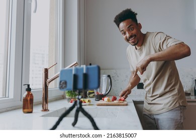 Young African American Man In Casual Clothes Prepare Sweet Breakfast Cut Fruit Do Selfie Shot Mobile Cell Phone Show Cooking Food Process In Indoor Kitchen At Home Alone Healthy Diet Lifestyle Concept