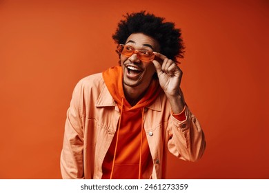 A young African American man with curly hair in trendy attire and sunglasses, showcasing emotions against an orange background. - Powered by Shutterstock