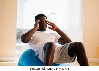 Young African American Man Doing Sit-up Exercise With Swiss Ball At Gym. Male Fitness Model Performing A Crunch At Fitness Center