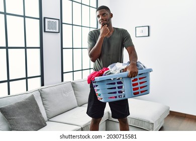 Young african american man doing laundry holding basket serious face thinking about question with hand on chin, thoughtful about confusing idea  - Powered by Shutterstock