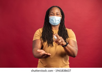 Young African American man with dreadlocks wearing protective face mask standing isolated on red wall background and spraying holding sanitizer before work, hygiene and safety concept during covid-19 - Powered by Shutterstock