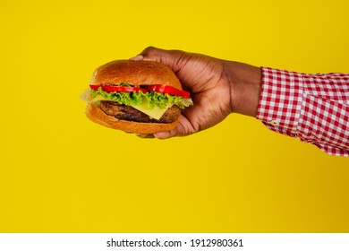 young african american man eating hamburger isolated on yellow background hands close up