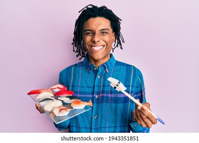 Young african american man eating sushi using chopsticks smiling with a happy and cool smile on face. showing teeth. 