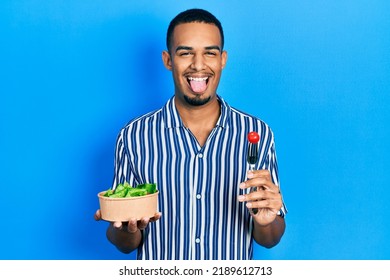 Young African American Man Eating Salad Sticking Tongue Out Happy With Funny Expression. 