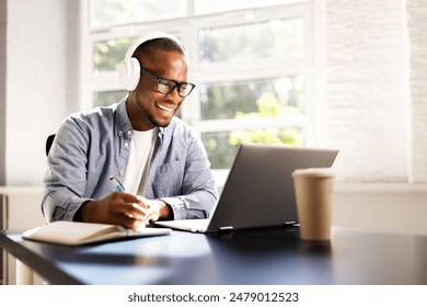 Young African American man excels in online education, studying with laptop and headphones for tests and joining virtual webinars. - Powered by Shutterstock