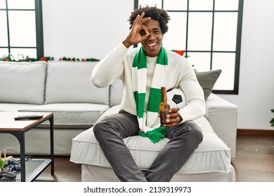 Young african american man football hooligan drinking beer cheering game smiling happy doing ok sign with hand on eye looking through fingers  - Shutterstock ID 2139319973