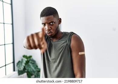 Young African American Man Getting Vaccine Showing Arm With Band Aid Pointing With Finger To The Camera And To You, Confident Gesture Looking Serious 