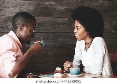 Young African American Man In Glasses Drinking Cappuccino With His Beautiful Girlfriend. Happy Stylish Friends Having Coffee Together, Sitting At A Cafe, Laughing And Having A Great Time Together