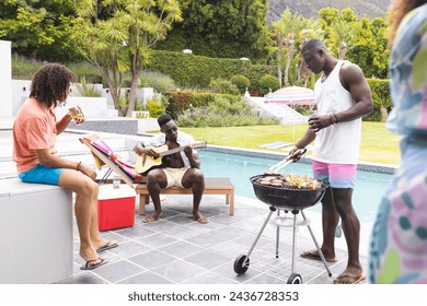 Young African American man grills food as another plays guitar by the pool. Biracial woman enjoys a meal, creating a relaxed outdoor gathering atmosphere. - Powered by Shutterstock