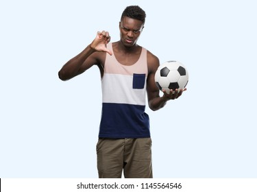 Young African American Man Holding Soccer Football Ball With Angry Face, Negative Sign Showing Dislike With Thumbs Down, Rejection Concept