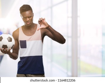 Young African American Man Holding Soccer Football Ball With Angry Face, Negative Sign Showing Dislike With Thumbs Down, Rejection Concept