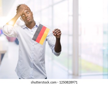 Young african american man holding german flag stressed with hand on head, shocked with shame and surprise face, angry and frustrated. Fear and upset for mistake. - Powered by Shutterstock