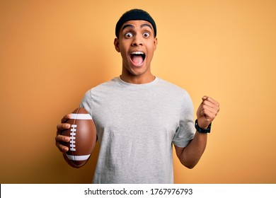 Young african american man holding rugby ball over isolated yellow background screaming proud and celebrating victory and success very excited, cheering emotion - Powered by Shutterstock