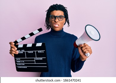 Young African American Man Holding Video Film Clapboard And Megaphone Clueless And Confused Expression. Doubt Concept. 