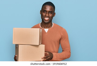 Young african american man holding delivery package looking positive and happy standing and smiling with a confident smile showing teeth 