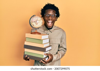 Young African American Man Holding A Pile Of Books And Vintage World Ball Celebrating Crazy And Amazed For Success With Open Eyes Screaming Excited. 