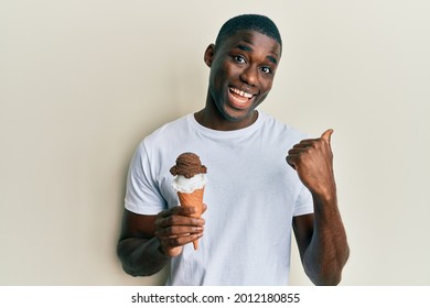 Young african american man holding ice cream pointing thumb up to the side smiling happy with open mouth  - Shutterstock ID 2012180855